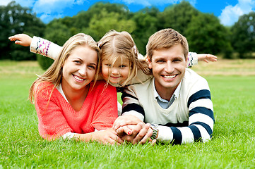 Image showing Couple lying in park with their daughter on top
