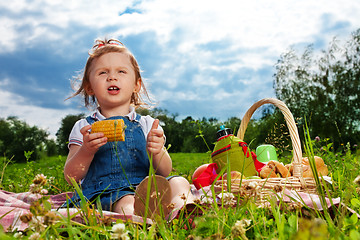 Image showing Thoughtful girl eating corn on picnic