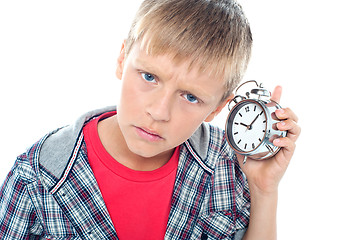 Image showing Confused young kid holding time piece close to his ear