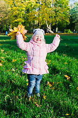 Image showing The little girl collects fallen down leaves in autumn park