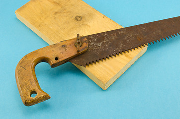 Image showing retro rusty hand saw and wood board part on blue 