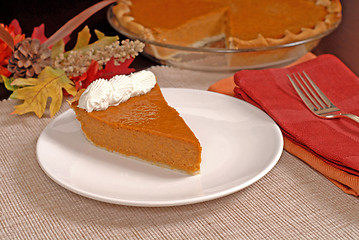 Image showing Slice of pumpkin pie with autumn leaves resting in background