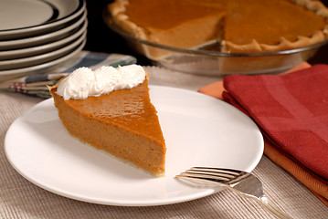 Image showing Slice of pumpkin pie with extra plates resting in background alo