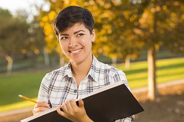 Image showing Mixed Race Young Female Holding Sketch Book and Pencil Outdoors