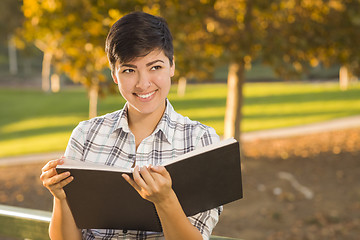 Image showing Mixed Race Young Female Holding Open Book and Pencil Outdoors