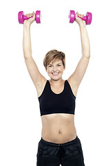 Image showing Mid adult woman holding dumbbells over head