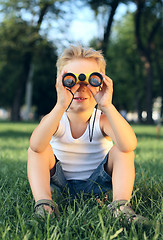 Image showing Little boy sitting in the park with a binoculars