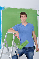 Image showing handsome young man paint white wall in color