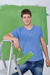 Image showing handsome young man paint white wall in color