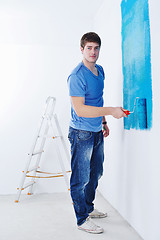 Image showing handsome young man paint white wall in color