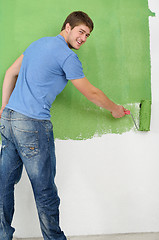 Image showing handsome young man paint white wall in color