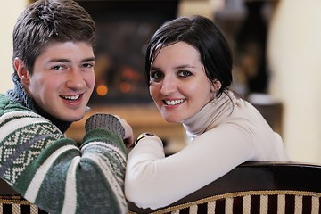 Image showing Young romantic couple sitting on sofa in front of fireplace at h