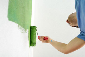 Image showing handsome young man paint white wall in color