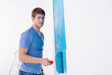 Image showing handsome young man paint white wall in color