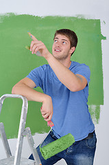 Image showing handsome young man paint white wall in color