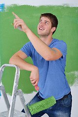 Image showing handsome young man paint white wall in color