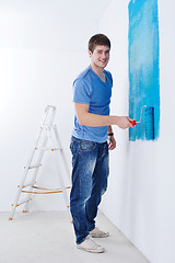 Image showing handsome young man paint white wall in color