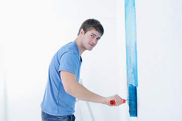 Image showing handsome young man paint white wall in color