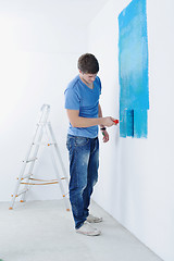 Image showing handsome young man paint white wall in color