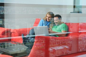 Image showing happy couple have fun and work on laptop at home on red sofa