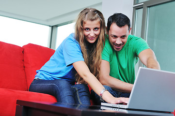 Image showing happy couple have fun and work on laptop at home on red sofa