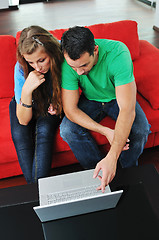 Image showing happy couple have fun and work on laptop at home on red sofa