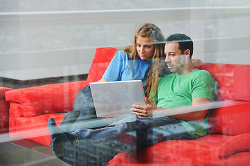 Image showing happy couple have fun and work on laptop at home on red sofa