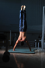 Image showing young man performing handstand in fitness studio