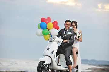 Image showing just married couple on the beach ride white scooter