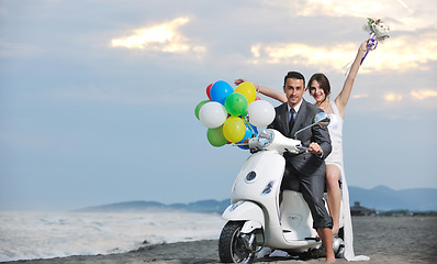 Image showing just married couple on the beach ride white scooter