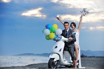 Image showing just married couple on the beach ride white scooter