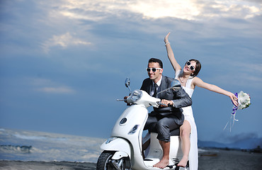 Image showing just married couple on the beach ride white scooter