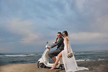 Image showing just married couple on the beach ride white scooter