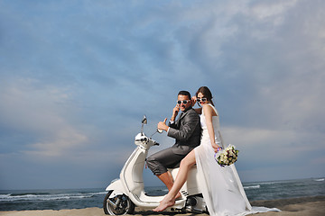 Image showing just married couple on the beach ride white scooter