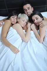Image showing Young handsome man lying in bed with three girls