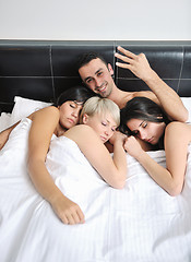 Image showing Young handsome man lying in bed with three girls