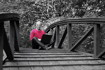 Image showing young businessman in red shirt working on laptop at bridge