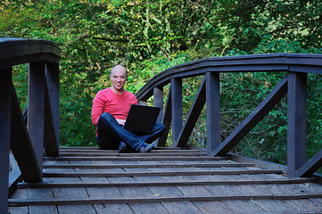 Image showing young businessman in red shirt at bridge  working on laptop 