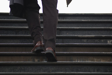 Image showing business executive climbing up stairs with umbrela in his hand