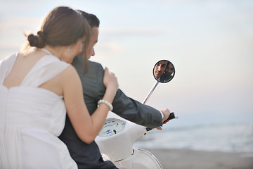 Image showing just married couple on the beach ride white scooter