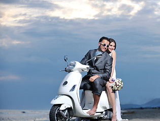 Image showing just married couple on the beach ride white scooter