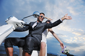 Image showing just married couple on the beach ride white scooter