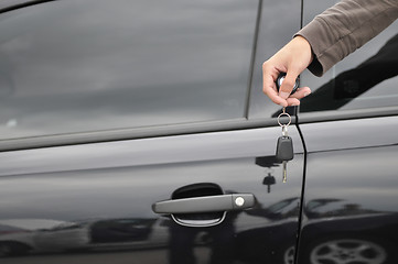 Image showing male hand holding car key with new black car in background