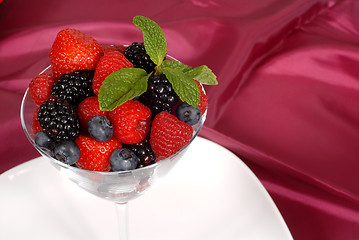 Image showing Fresh berries topped with mint in a martini glass resting on a w