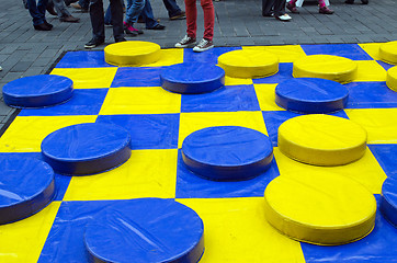 Image showing outdoor checkers game figures yellow blue people 