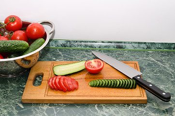 Image showing red tomato and green cucumbers slices with knife on board