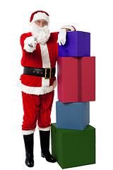 Image showing Smiling senior Santa posing beside colorful stack of Xmas presents