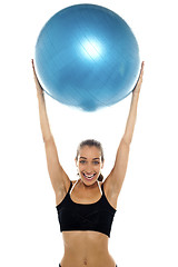 Image showing Fit young lady holding up big blue pilates ball