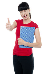 Image showing Pretty teenager holding notebook and gesturing thumbs up