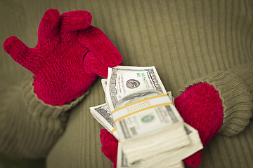 Image showing Woman Wearing Mittens Holding Stacks of Money with Red Ribbon